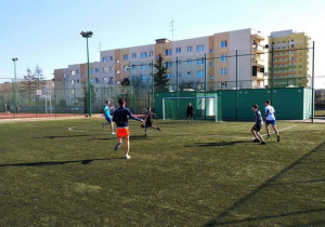 Uczniowie grają w piłkę nożną na boisku.