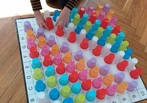 Uczeń układa kubeczkowe sudoku na planszy. Kubeczki są ustawione kolorami w rzędach. Kubeczki wypełniają wszystkie pola na planszy.