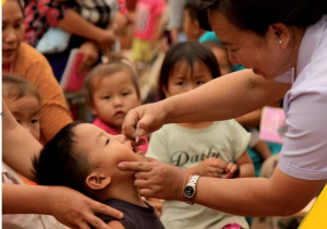 Pielęgniarka podaje małemu chłopcu szczepionkę w postaci kropelek. Napis: Szczepienia ratują życie dzieci na całym świecie! UNICEF dla każdego dziecka.