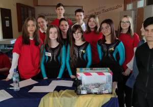 Grupa uczniów - chłopcy i dziewczynki - pozują do zdjęcia przy stole, na którym stoi pudełko ze zbieranymi pieniędzmi.