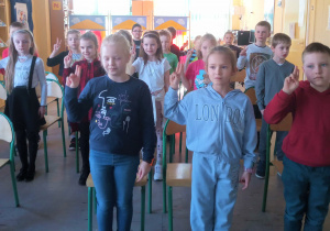 Grupa uczniów stoi w sali bibliotecznej. Mają wzniesione do góry dwa palce i składają przysięgę.