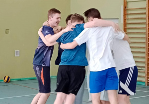 Zawodnicy z klasy 8c wykonują taniec zwycięstwa wykonany po wygranym meczu. Chłopcy stoją w kręgu i trzymając się za ramiona podskakują do góry.