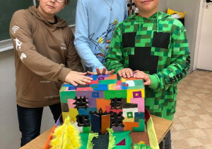 Trzech uczniów prezentuje swoją pracę - makietę Akademii wykonaną z tekturowych kartonów, pomalowanych farbą i oklejonych kolorową bibułą
