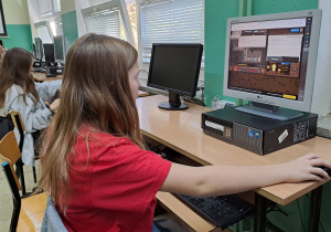 Uczniowie klasy 8 siedzą przed komputerami w sali informatycznej. Uczennica na pierwszym planie koduje w języku Python.