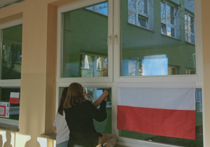 Uczennice przyklejają dekoracje do okien w holu szkolnym.