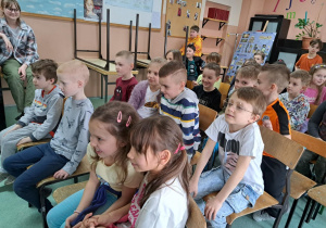 Uczniowie siedzą na krzesłach w kilku rzędach.