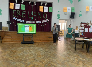 Nauczycielka rozpoczyna Międzyszkolny Turniej Języka angielskiego. Po środku sali stoi monitor interaktywny. Za monitorem rozwieszona dekoracja z napisem Ireland.