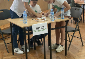 Uczniowie Szkoły Podstawowej nr 12 rozwiązują zadania konkursowe przy stoliku.