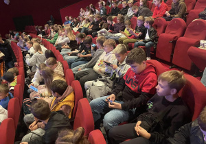 Uczniowie Szkoły Podstawowej nr 12 siedzą w rzędach sali kinowej.