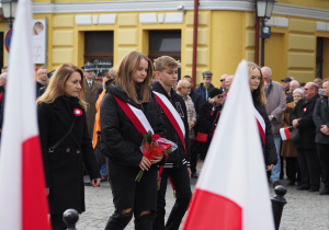Nauczycielki i uczniowie Szkoły Podstawowej nr 12 w Koninie stoją pod pomnikiem Józefa Piłsudskiego.