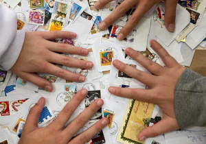 Znaczki pocztowe rozsypane na stole. Cztery dłonie dzieci dotykają znaczki.