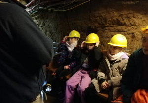 Uczennice siedzą na ławce w podziemnym korytarzu kopalni. Na głowach mają żółte kaski.