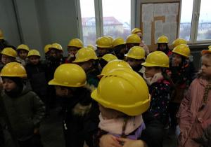 W pomieszczeniu stoi tyłem duża grupa dzieci. Wszystkie na głowach mają żółte kaski.