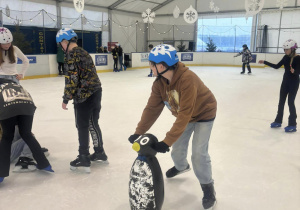 Uczniowie jadą na łyżwach i podpierają się pingwinami.