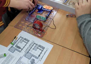 Uczniowie budują obwód elektryczny według instrukcji. Na stole jest zestaw elektryczny Boffin.