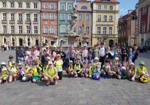 Duża grupa dzieci stoi przed zabytkowym pomnikiem. W tle widać zabytkowe kamienice.