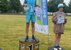 Na podium dzieci maja medale, trzymają nagrody, dyplom. W tle trawa o stadion.