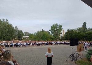 Uczniowie znajdują się na placu apelowym szkoły. Trwa rozpoczęcie roku szkolnego. Pani dyrektor przemawia.