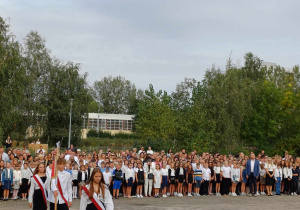 Szkolny poczet sztandarowy idzie na placu apelowym szkoły. Wszyscy uczniowie stoją na baczność w oczekiwaniu na zaśpiewanie hymnu państwowego.