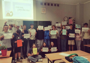 Uczniowie z wychowawczynią trzymają kolorowe kartki z hasłami promującymi pozytywne myślenie.