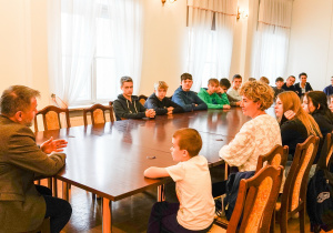 Uczniowie, nauczycielki, prezydenta miasta siedzą przy długim, brązowym stole w gabinecie prezydenta.