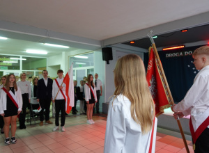 Uczniowie ubrani na galowo ze sztandarem. Uczniowie z biało - czerwoną flagą.