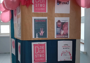 Na sciance wiszą kolorowe plakaty, zawierające informacje dotyczące kampanii. Nad nimi wiszą czerwone balony.
