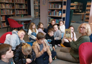 Uczniowie siedzą na dywanie, nauczyciel czyta dla nich książkę.