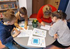 Uczniowie rozwiązują przygotowane zadania. Siedzą przy okrągłym stoliku, na którym leżą kartki z zadaniami.