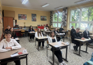 Uczniowie siedzą w ławkach, czekają na rozpoczęcie egzaminu.