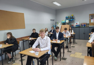 Uczniowie siedzą w ławkach, czekają na rozpoczęcie egzaminu.
