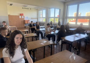 Uczniowie siedzą w ławkach, czekają na rozpoczęcie egzaminu.