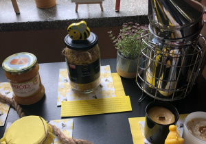 Na stoliku znajdują się miód, pyłek pszczeli, akcesoria pszczelarskie.