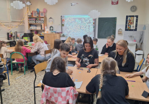 Uczniowie i rodzice siedzą przy stolikach i wykonują wspólnie zadania.