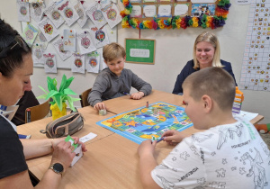 Uczniowie i rodzice siedzą przy stolikach i wykonują wspólnie zadania.