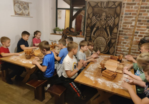 Uczniowie siedzą przy stolikach, z przygotowanego ciasta wykrawają różne kształty pierników.