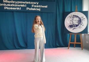 Uczennica stoi na scenie, trzyma w ręku mikrofon i śpiewa piosenkę konkursową.