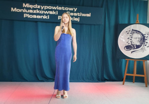 Uczennica stoi na scenie, trzyma w ręku mikrofon i śpiewa piosenkę konkursową.