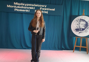 Uczennica stoi na scenie, trzyma w ręku mikrofon i śpiewa piosenkę konkursową.
