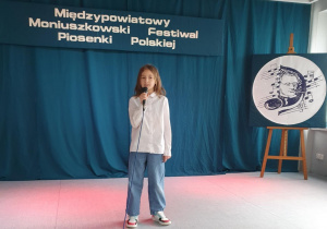 Uczennica stoi na scenie, trzyma w ręku mikrofon i śpiewa piosenkę konkursową.