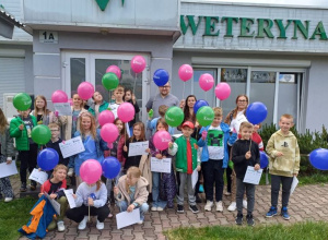 Uczniowie z kolorowymi balonami przed przychodnią weterynaryjna.