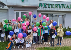 Uczniowie z kolorowymi balonami przed przychodnią weterynaryjna.