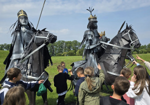 Uczniowie oglądają posągi rycerzy, wykonane z metalowego tworzywa.