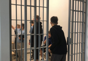 Uczniowie w areszcie, wchodzą do pomieszczenia za kratami.