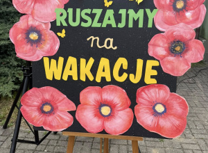 Gazetka z hasłem: Ruszajmy na wakacje. Na granatowym tle żółte i zielone litery, w koło czerwone maki.