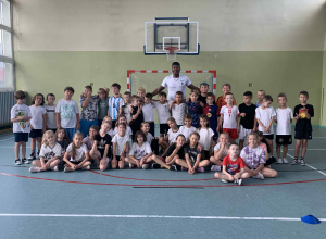 Uczniowie z koszykarzem na sali gimnstycznej.