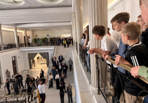 Uczniowie obserwują z balkonu znanych polityków w sejmie.