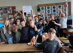 Uczniowie klasy z prezentami z Dnia Chłopca i butelkami napoju w ręku znajdują się w sali lekcyjnej.