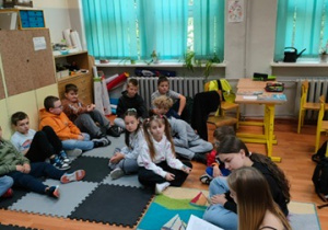 Uczennice czytają książkę dzieciom siedzącym na dywanie