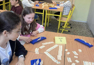 Grupa uczniów skupiona nad planszą podczas gry w Rummikub.